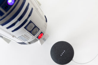 Science fiction meets science fact. Cinematic droid R2-D2 faces off with a Google Home Mini speaker and Google Assistant. Image: Digitized House Media.